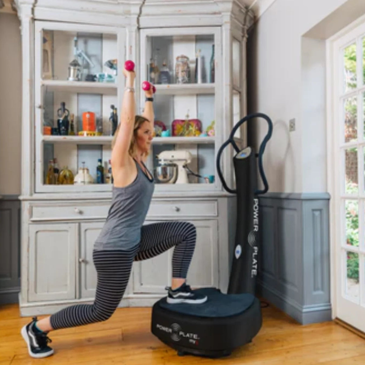 Woman exercising on a Power Plate machine in a home setting.